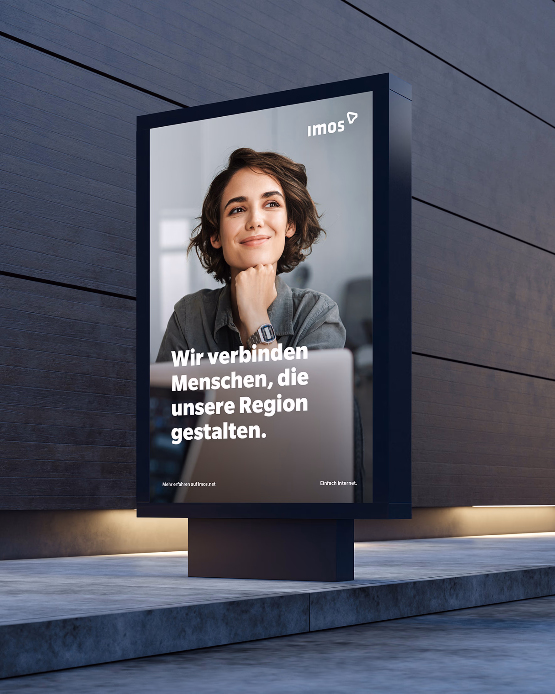 Nächtliche Plakatwerbung von imos mit dem Spruch „Wir verbinden Menschen, die unsere Region gestalten” an einer Gebäudefassade