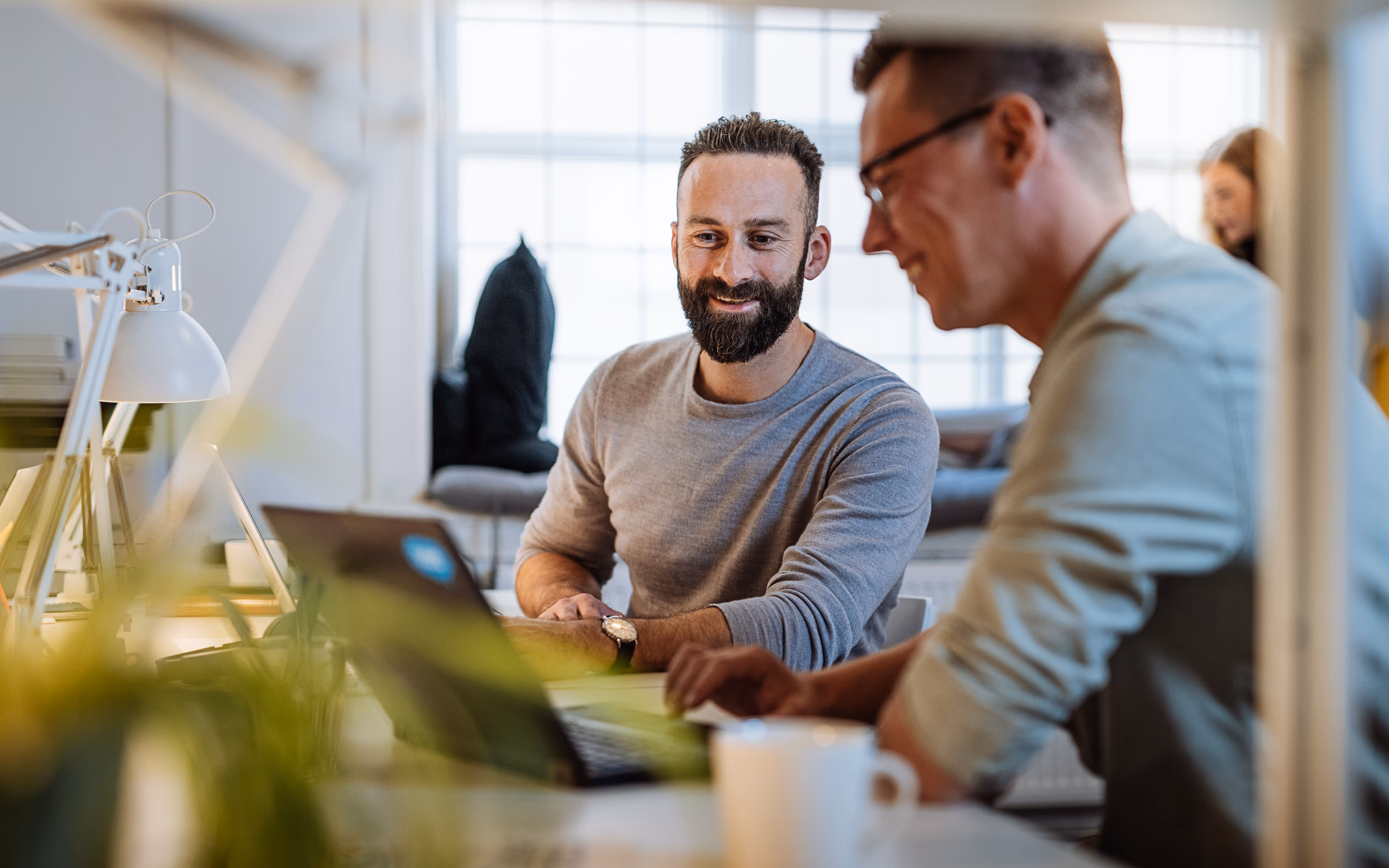 Zwei lächelnde Männer im Gespräch an einem Schreibtisch im Büro