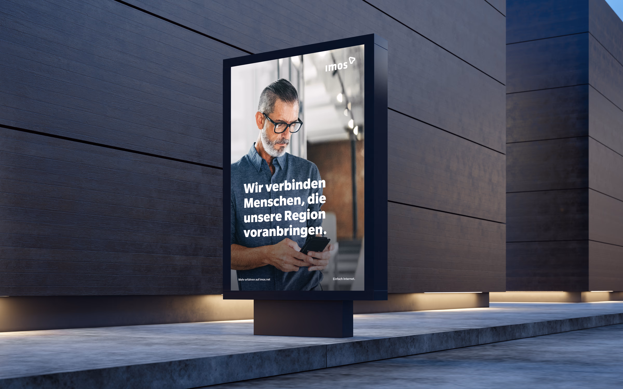 Beleuchtete Plakatwerbung von imos an einer Gebäudefassade bei Nacht